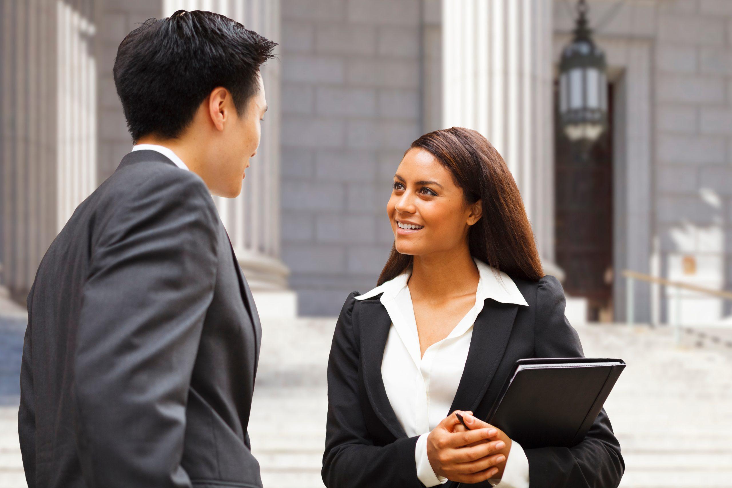 Two well dressed professionals in discussion outdoors in front of a government building.
